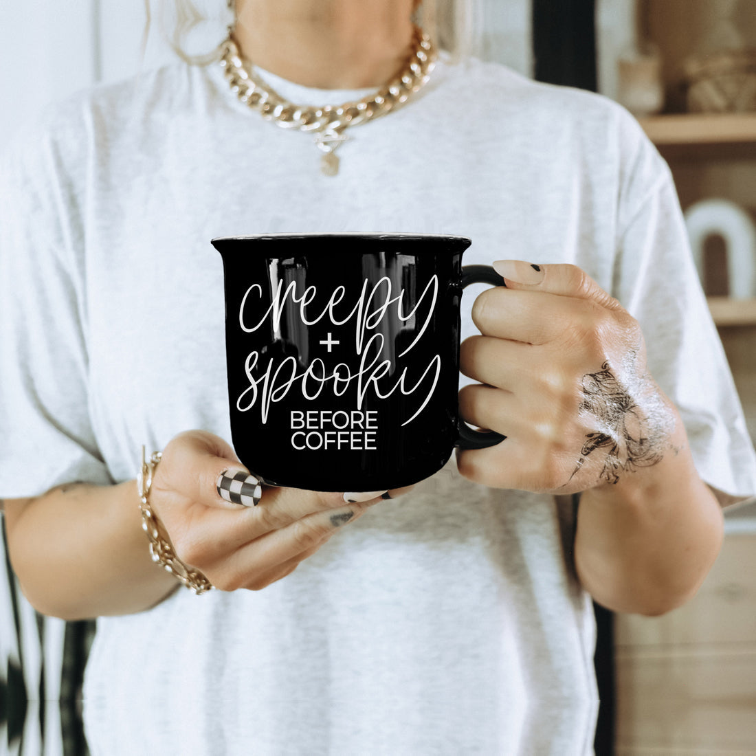Woman in a white tee holding the Creepy and Spooky Before Coffee mug