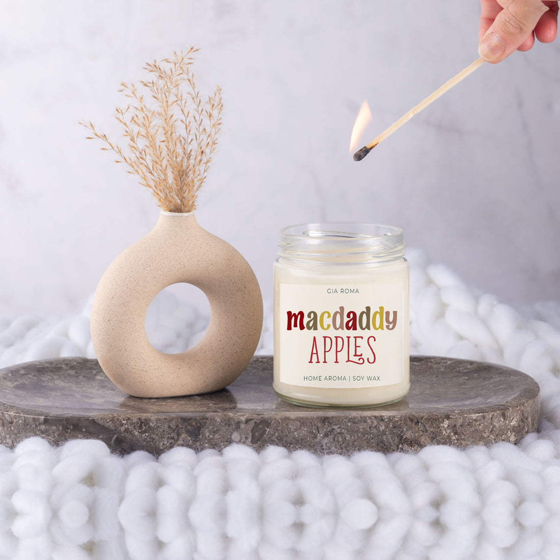 Macdaddy Apples candle beside a ring vase on a stone slab