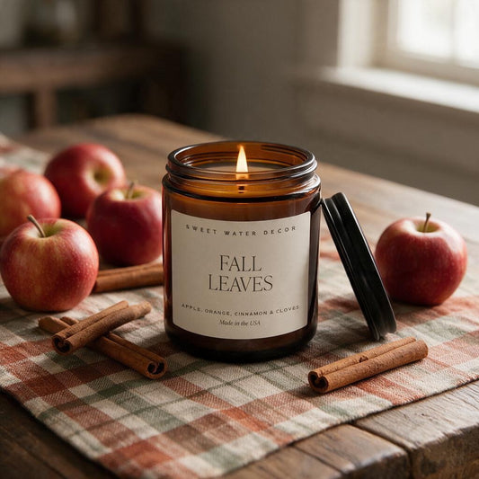 Lit Fall Leaves apple cinnamon soy candle in an amber glass jar on a plaid runner with red apples and cinnamon sticks
