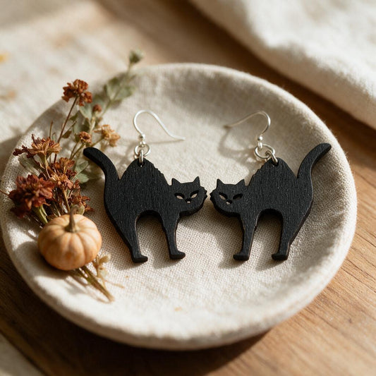 Black wooden scaredy cat earrings on a linen dish beside dried flowers and a mini pumpkin