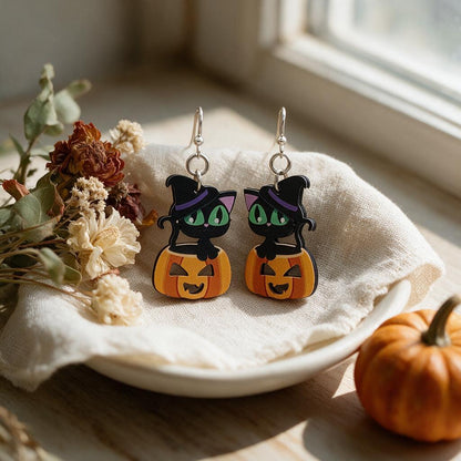 Black cat on jack-o-lantern wooden earrings on a linen dish beside dried flowers and a mini pumpkin