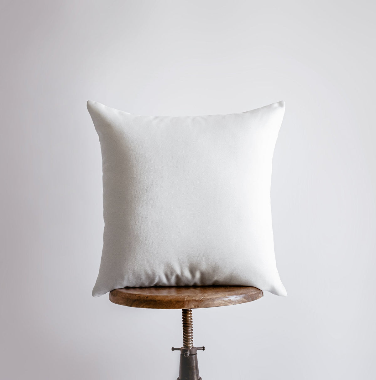 Plain white back of the Blessed throw pillow on a wooden stool