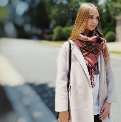 Woman wearing the pink and black braided fringe plaid scarf with a cream coat