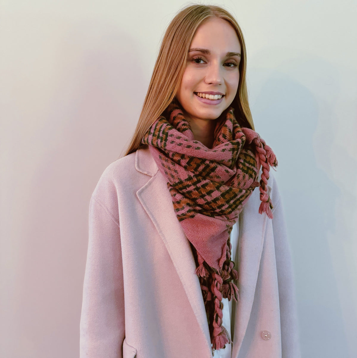 Woman wearing the pink plaid braided fringe scarf with a pink coat
