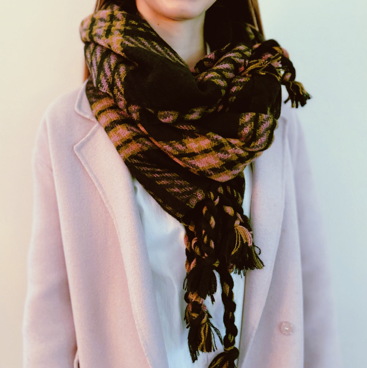 Black plaid scarf with braided tassels wrapped over a pink coat