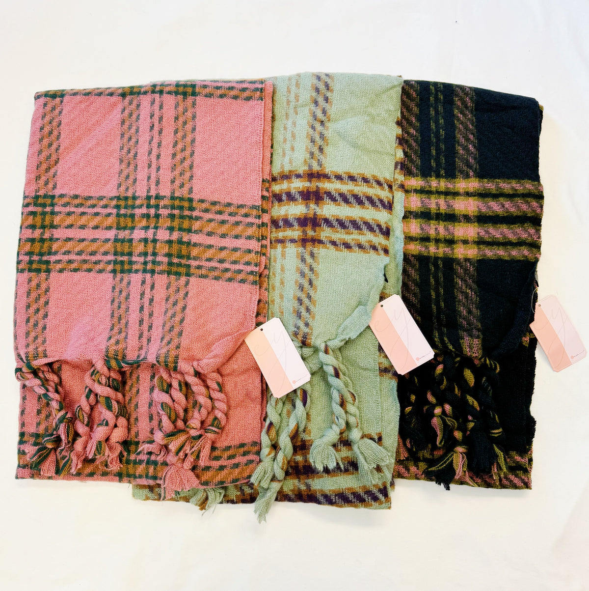 Braided fringe plaid scarves in pink, sage and black laid side by side
