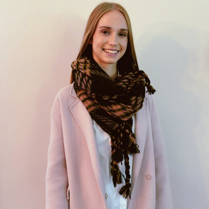 Woman wearing the black plaid braided fringe scarf with a pink coat