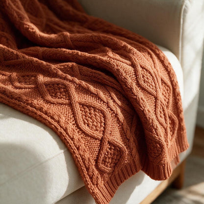 Close-up of the rust diamond cable knit texture and ribbed edge on the throw blanket draped over a cream sofa