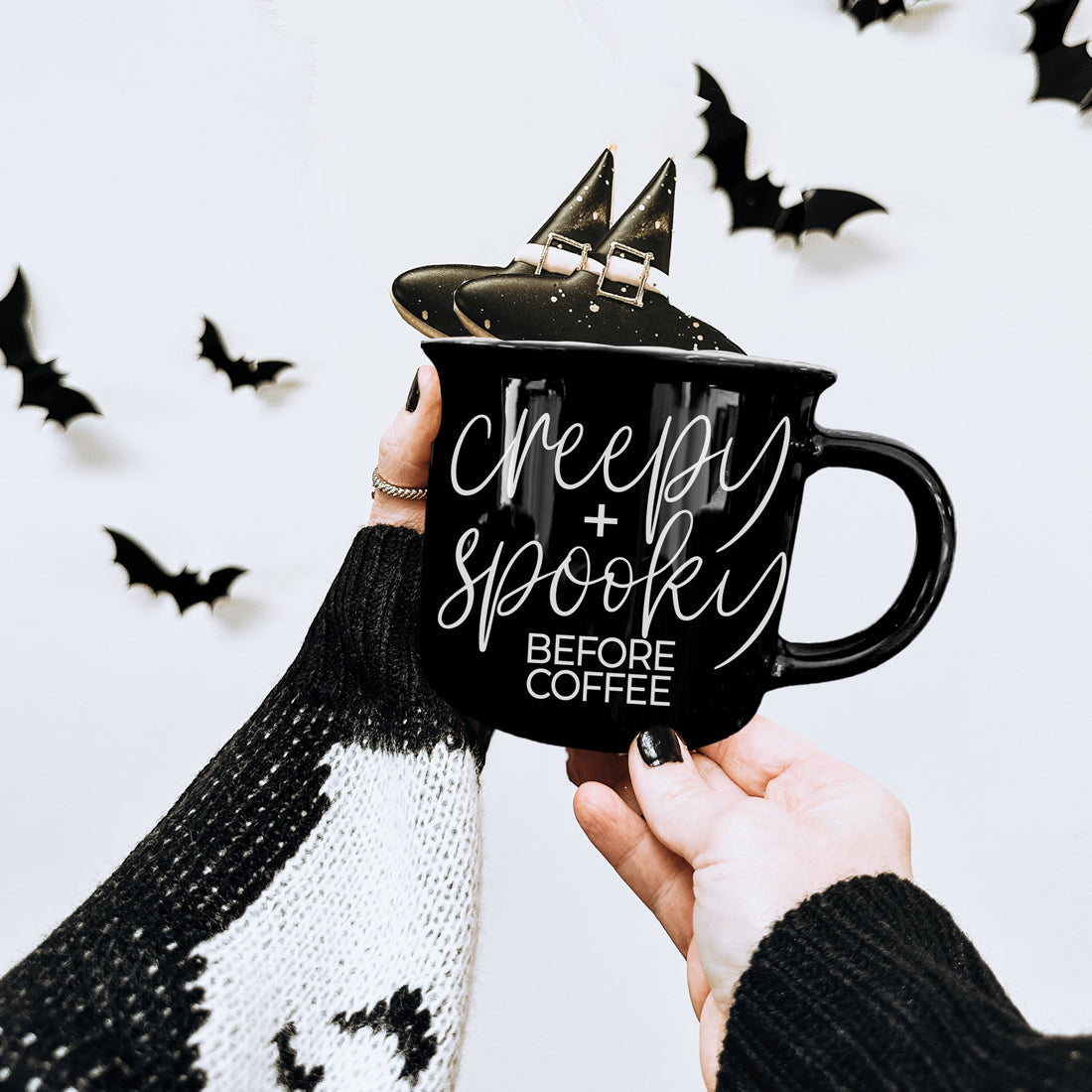 Black Creepy and Spooky Before Coffee mug held up with Halloween bats in the background