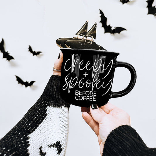 Black Creepy and Spooky Before Coffee mug held up with Halloween bats in the background