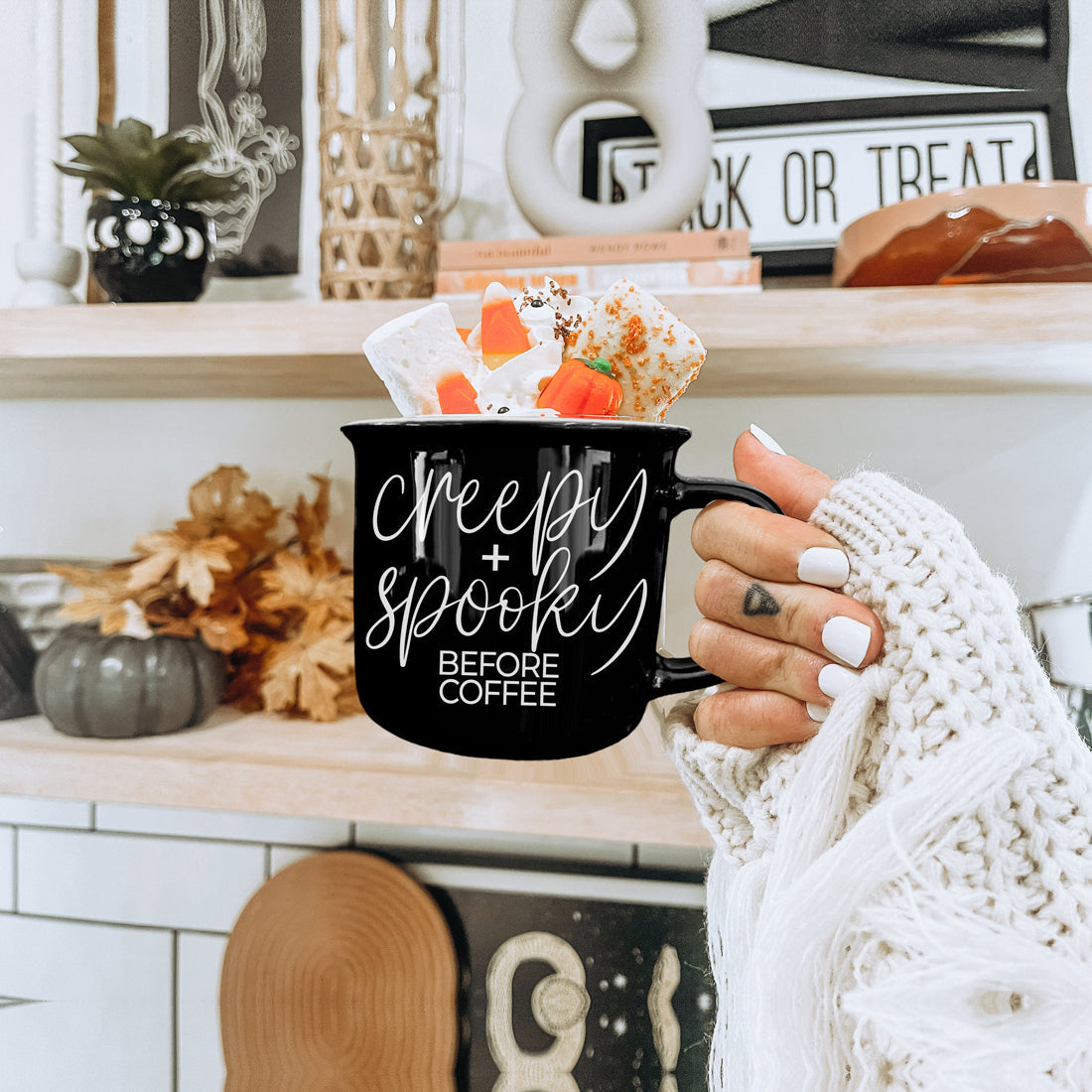 Creepy and Spooky mug with candy corn treats held by a hand in a cream knit sleeve