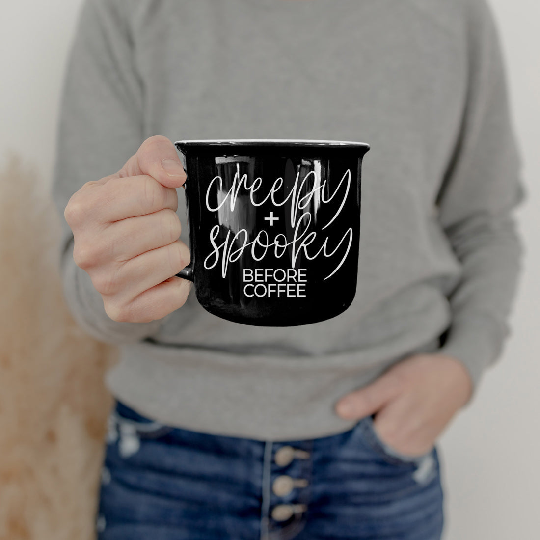 Creepy and Spooky mug held by a woman in a gray sweatshirt