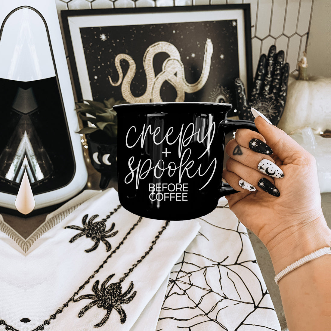 Creepy and Spooky Before Coffee mug held beside spider and snake Halloween decor