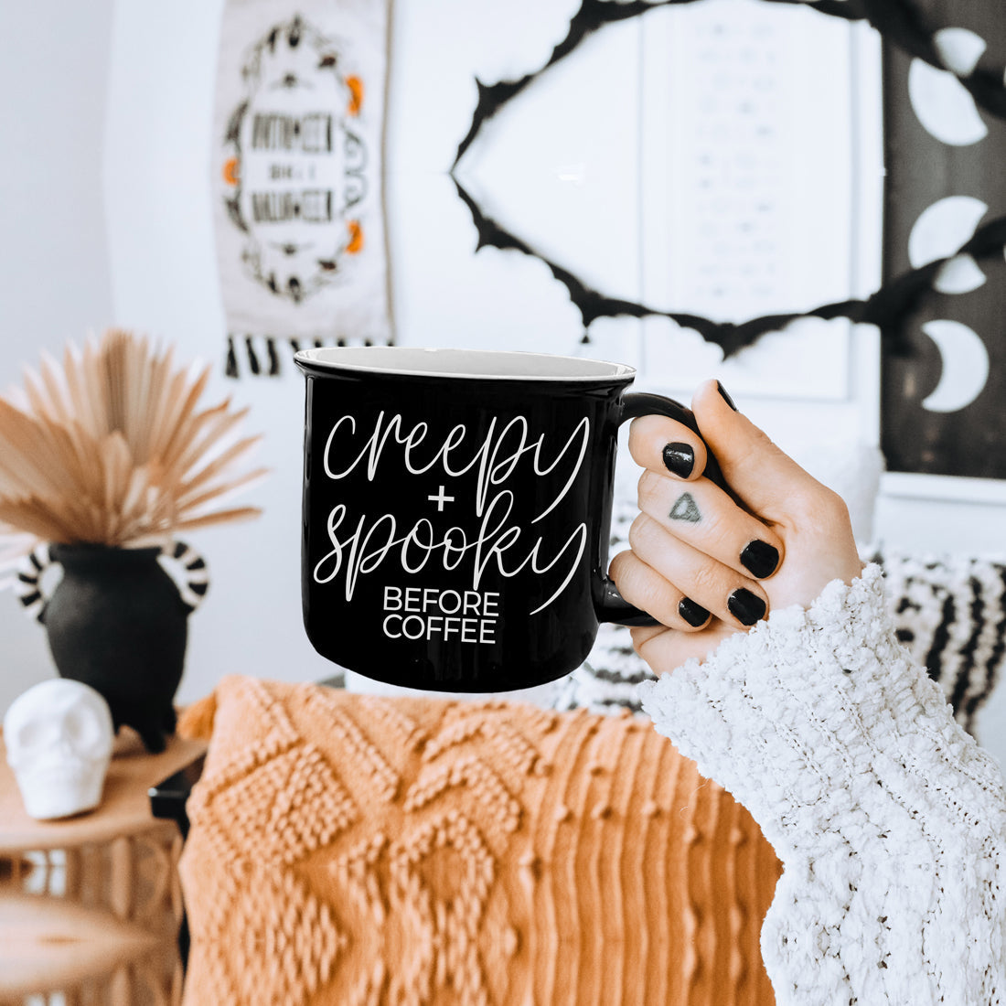 Creepy and Spooky Before Coffee mug held in front of boho Halloween decor