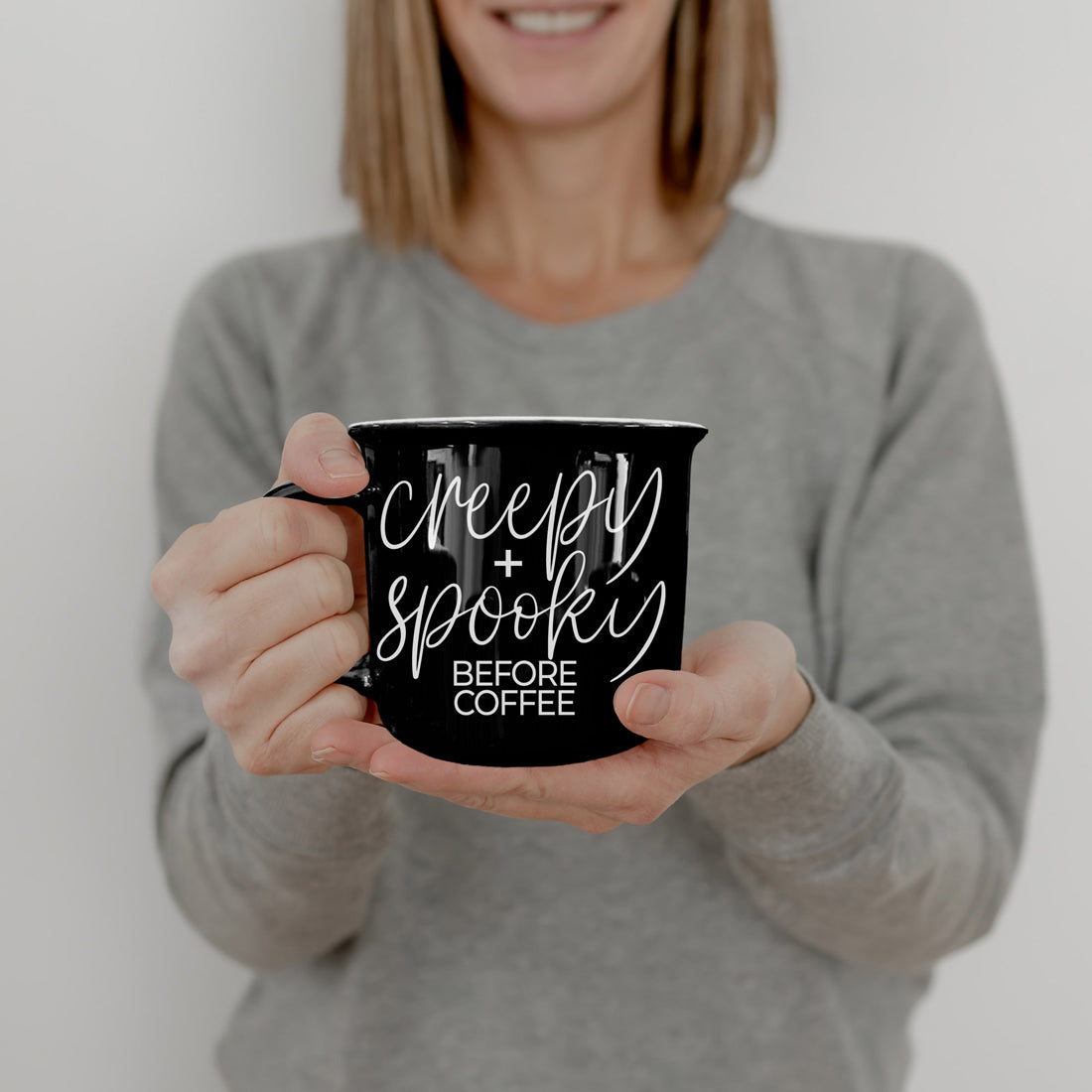 Woman in a gray sweater holding the Creepy and Spooky Before Coffee mug