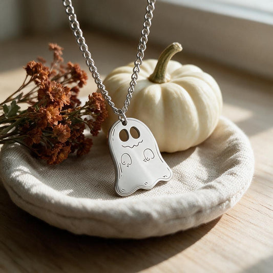 Silver ghost pendant necklace on a linen dish beside a white mini pumpkin
