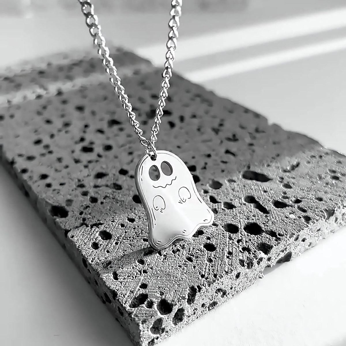 Silver cute ghost pendant on a chain resting on gray stone