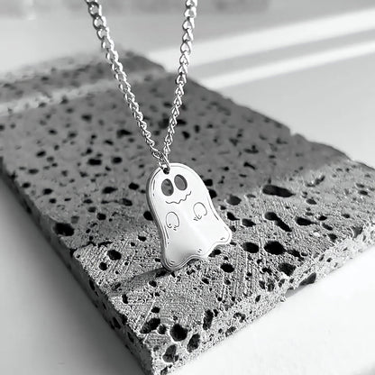 Silver cute ghost pendant on a chain resting on gray stone