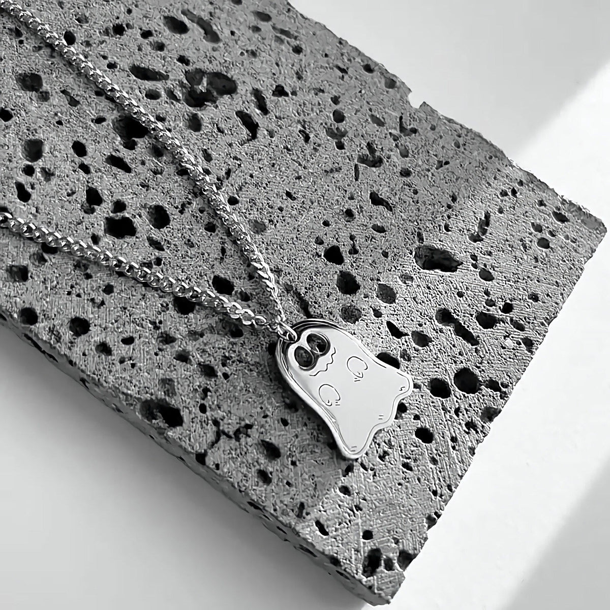 Silver ghost pendant necklace on a Cuban chain draped over gray stone