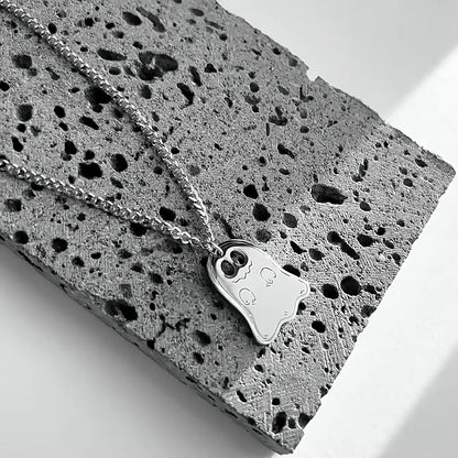 Silver ghost pendant necklace on a Cuban chain draped over gray stone