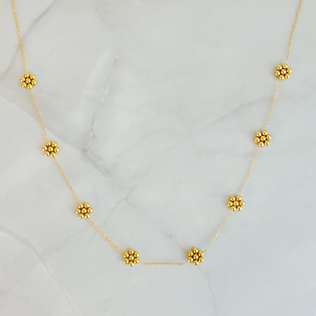 Dainty gold bead flower necklace laid out on white marble