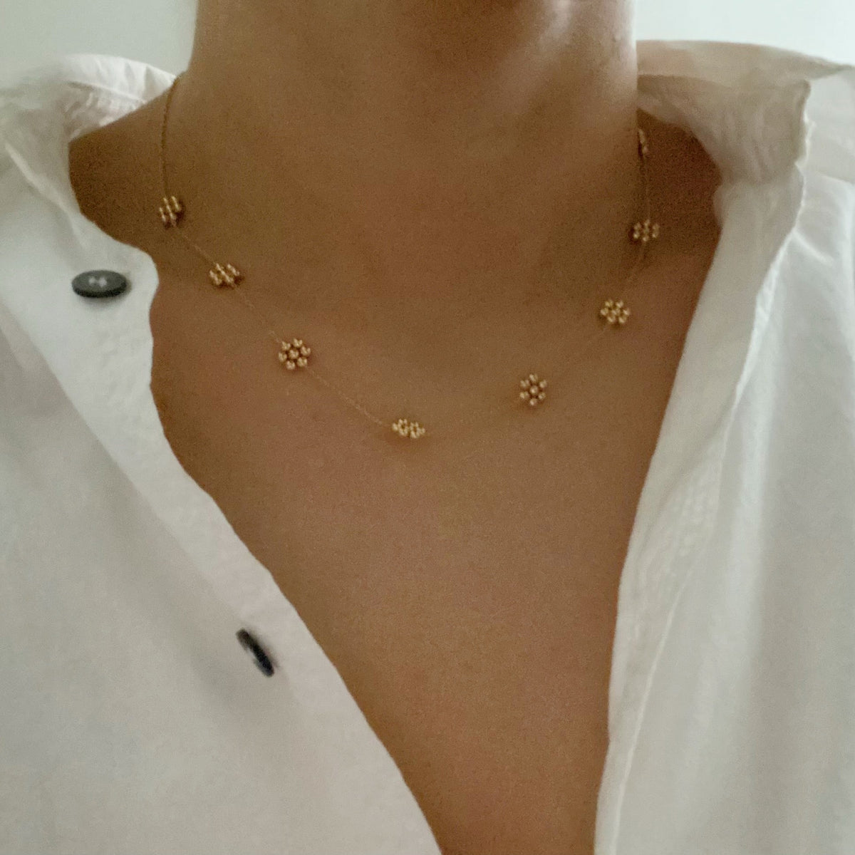 Gold bead flower necklace worn with an open white collared shirt
