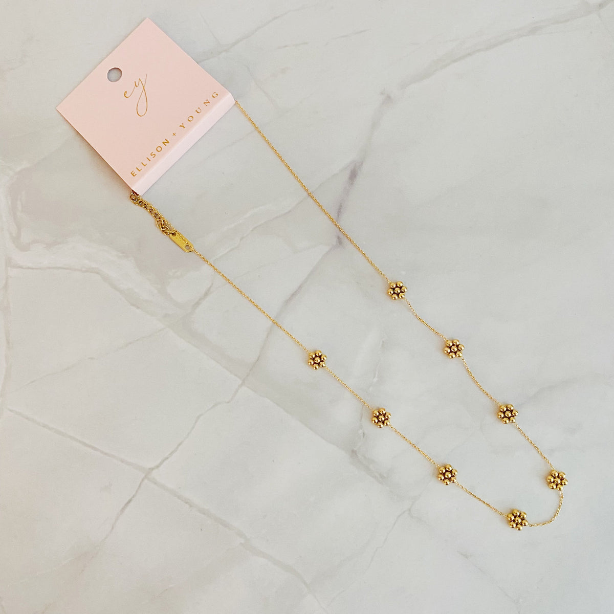 Gold bead flower necklace with its pink gift card and lobster clasp on marble