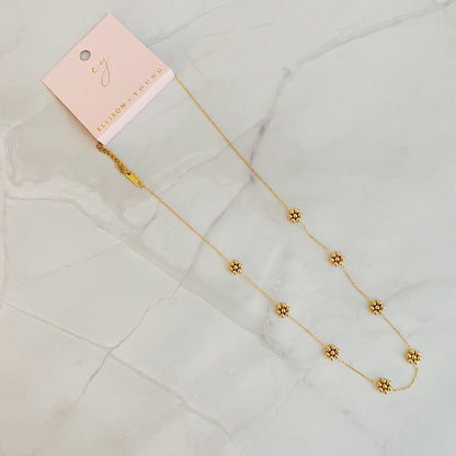 Gold bead flower necklace with its pink gift card and lobster clasp on marble