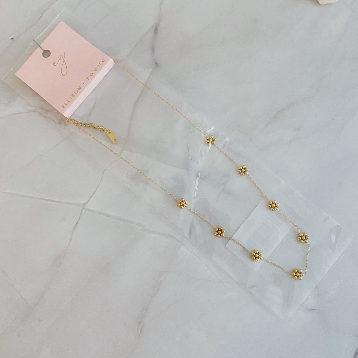 Gold bead flower necklace in its clear gift bag with a pink jewelry card