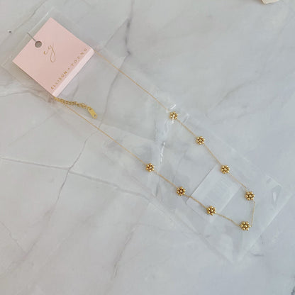 Gold bead flower necklace in its clear gift bag with a pink jewelry card