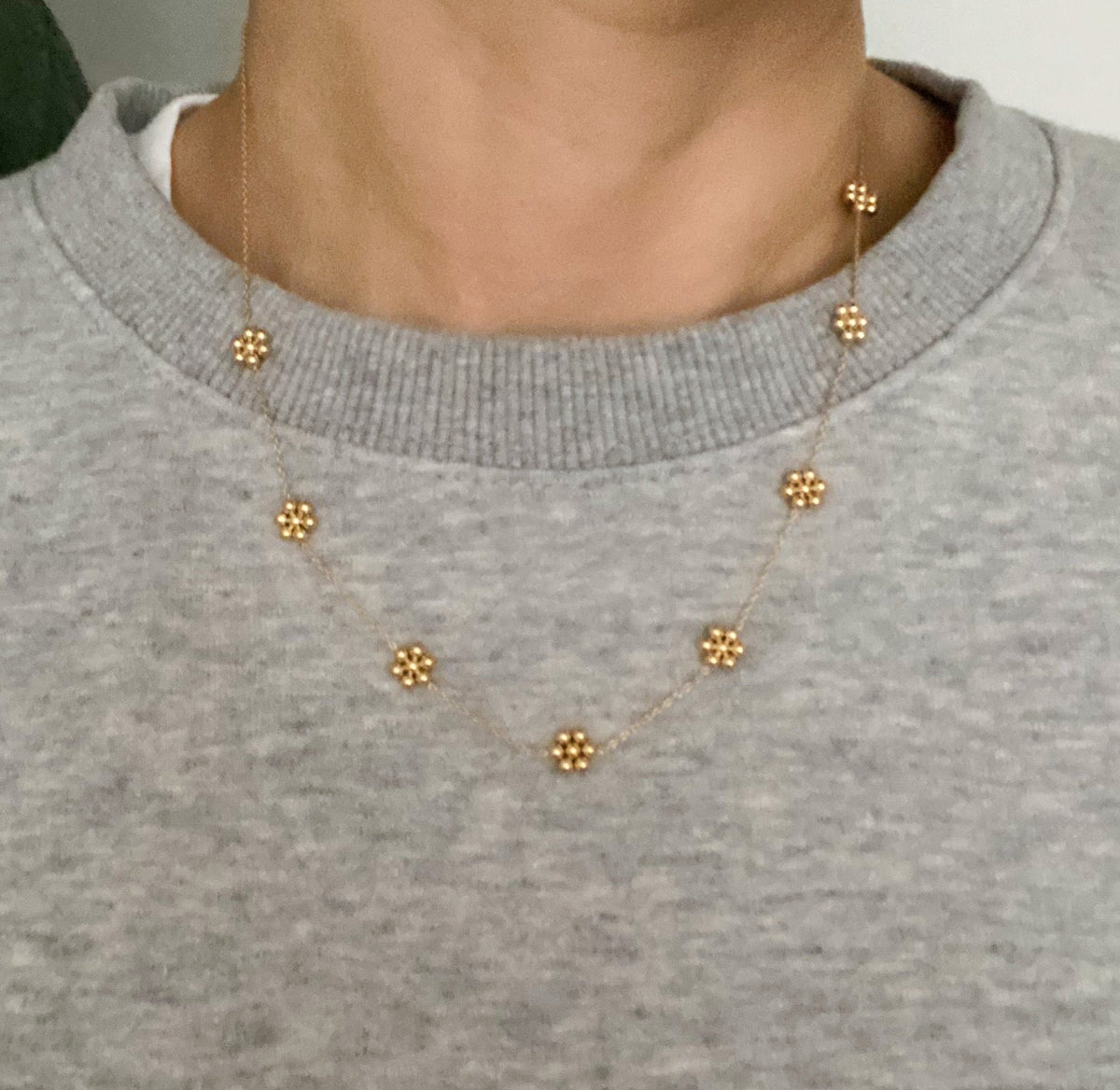 Dainty gold flower station necklace worn over a gray sweatshirt