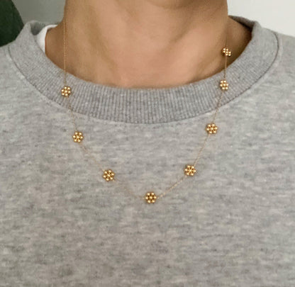 Dainty gold flower station necklace worn over a gray sweatshirt