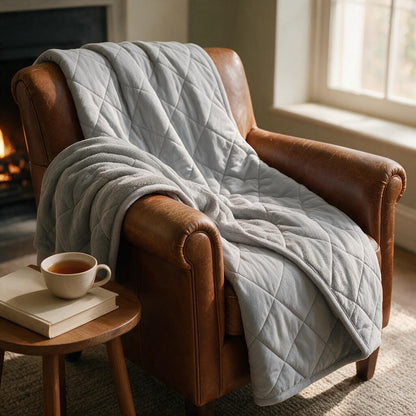 Grey quilted reversible blanket draped over a leather armchair by the fireplace