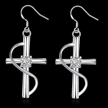 Pair of silver cross dangle earrings with crystal on a black background