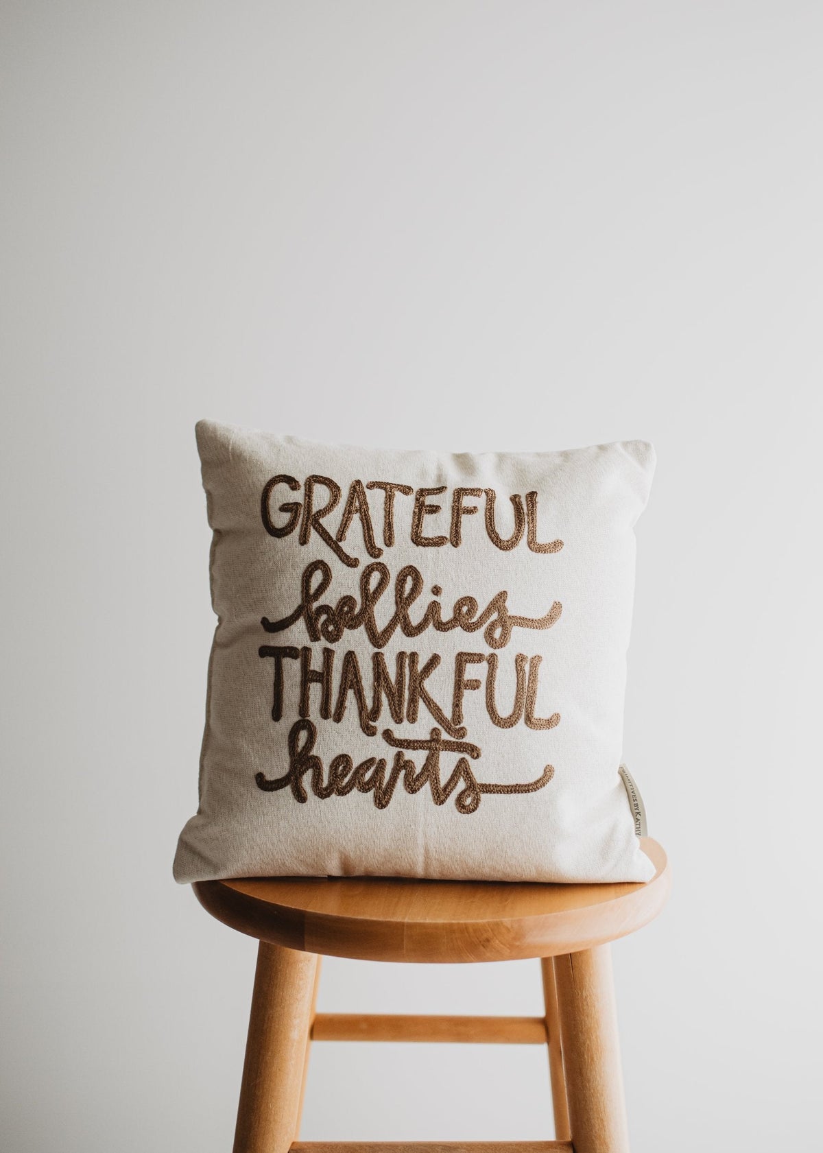 Grateful Bellies Thankful Hearts brown lettered throw pillow on a wooden stool