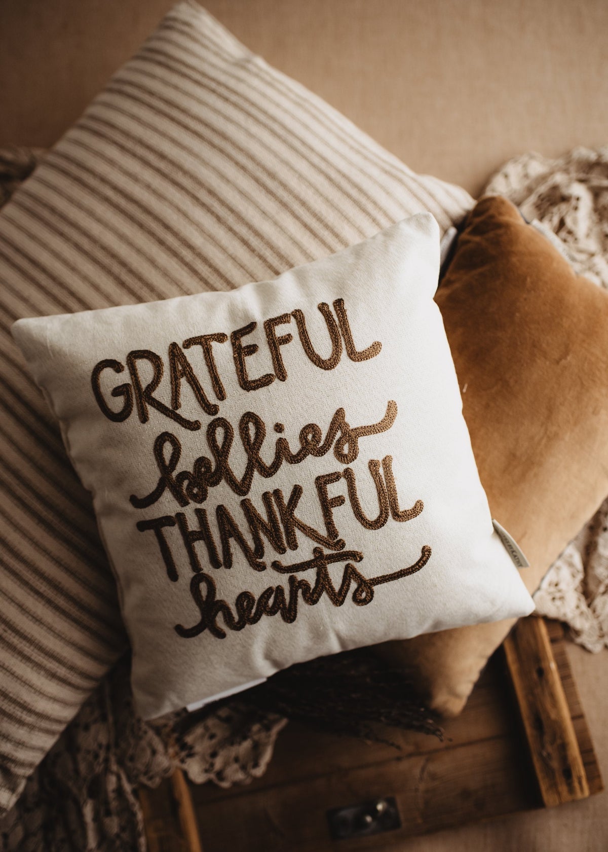 Close-up of the hand-lettered Grateful Bellies Thankful Hearts pillow with cozy throws