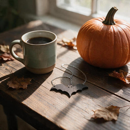 Wooden bat pendant necklace on a rustic wood table beside a coffee mug and pumpkin, shown at true 3.5-inch size