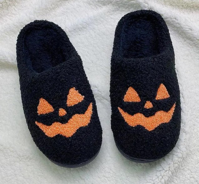 Pair of black fuzzy slippers with orange jack-o-lantern faces