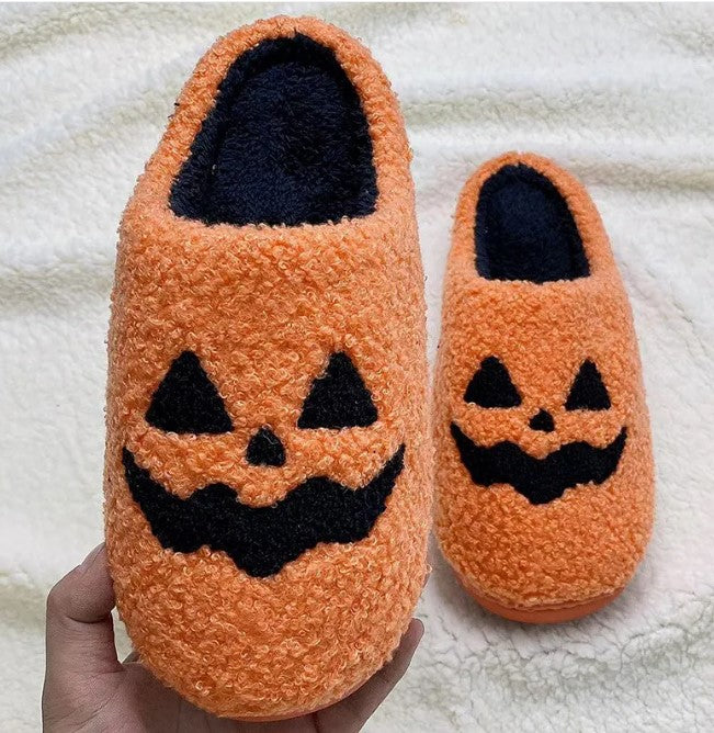 Orange fuzzy jack-o-lantern slippers held up to show size