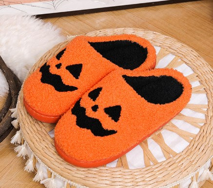 Orange jack-o-lantern fuzzy slippers on a woven rattan mat