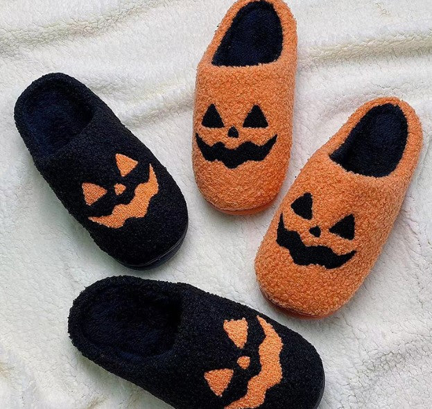 Black and orange jack-o-lantern fuzzy slippers on a white rug
