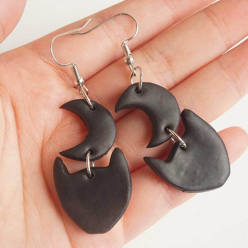 Black moon and cat clay earrings held in a hand
