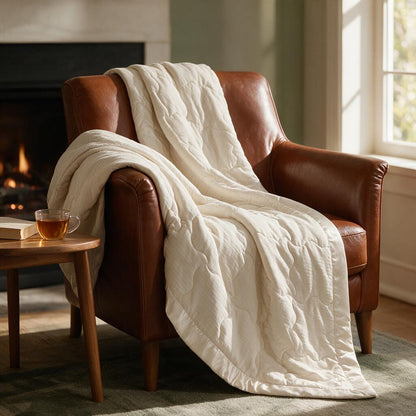 Ivory quilted blanket with satin trim draped over a leather armchair by the fireplace