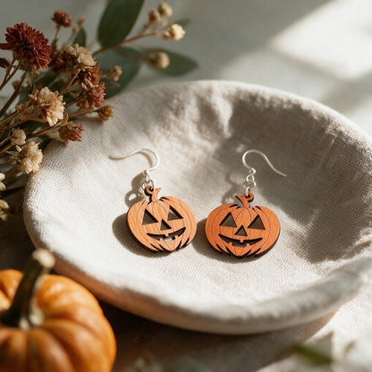 Orange wooden jack-o-lantern earrings shown at true 1.27-inch size on a linen dish beside dried flowers and a mini pumpkin