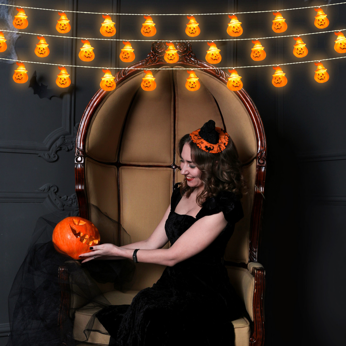Pumpkin string lights hung above a woman holding a jack-o-lantern
