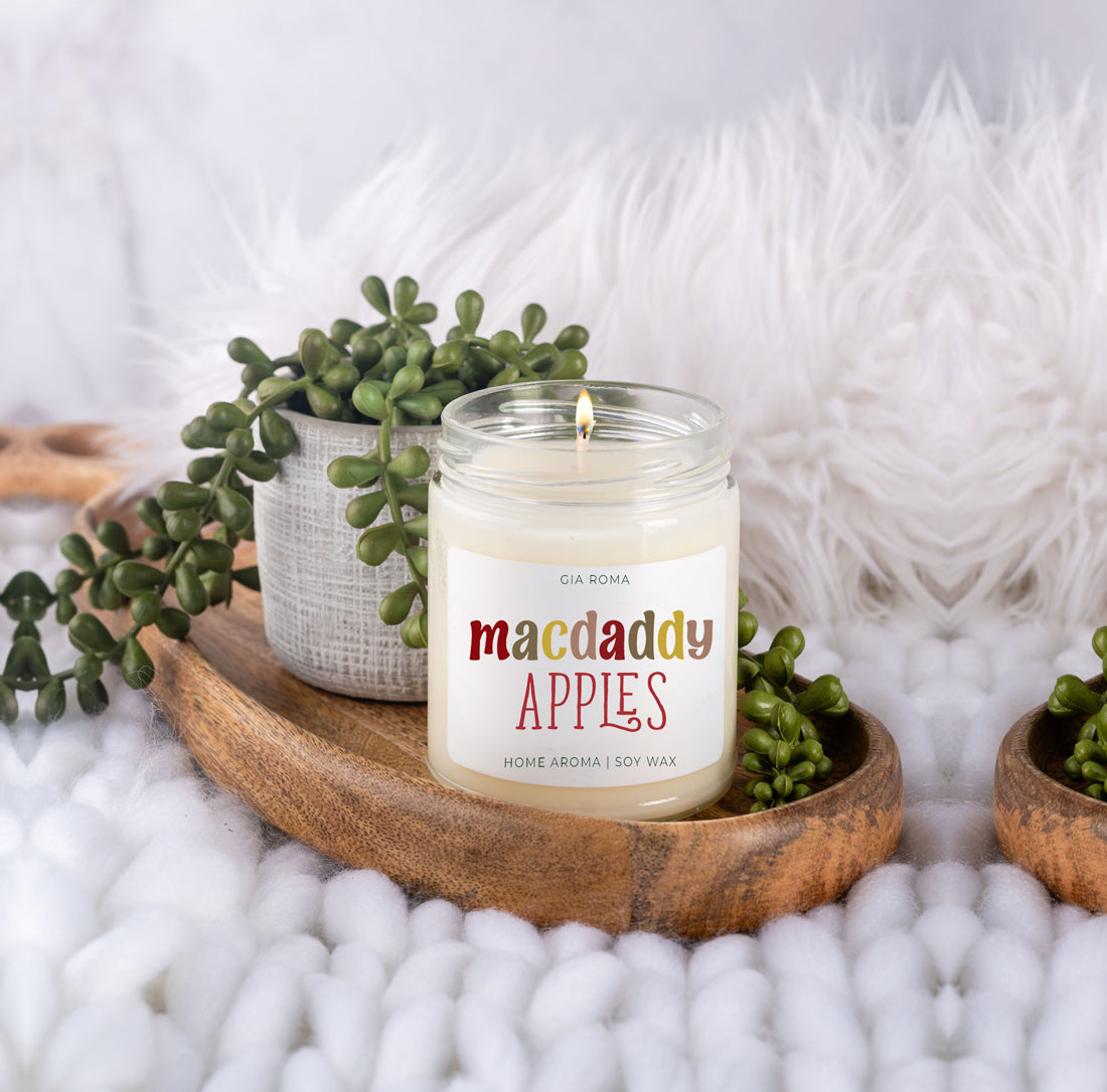 Lit Macdaddy Apples candle on a wood tray with greenery