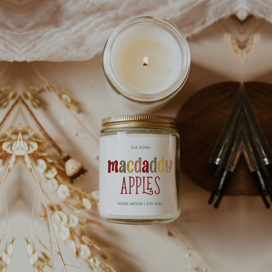 Macdaddy Apples candle with a lit candle and dried grasses