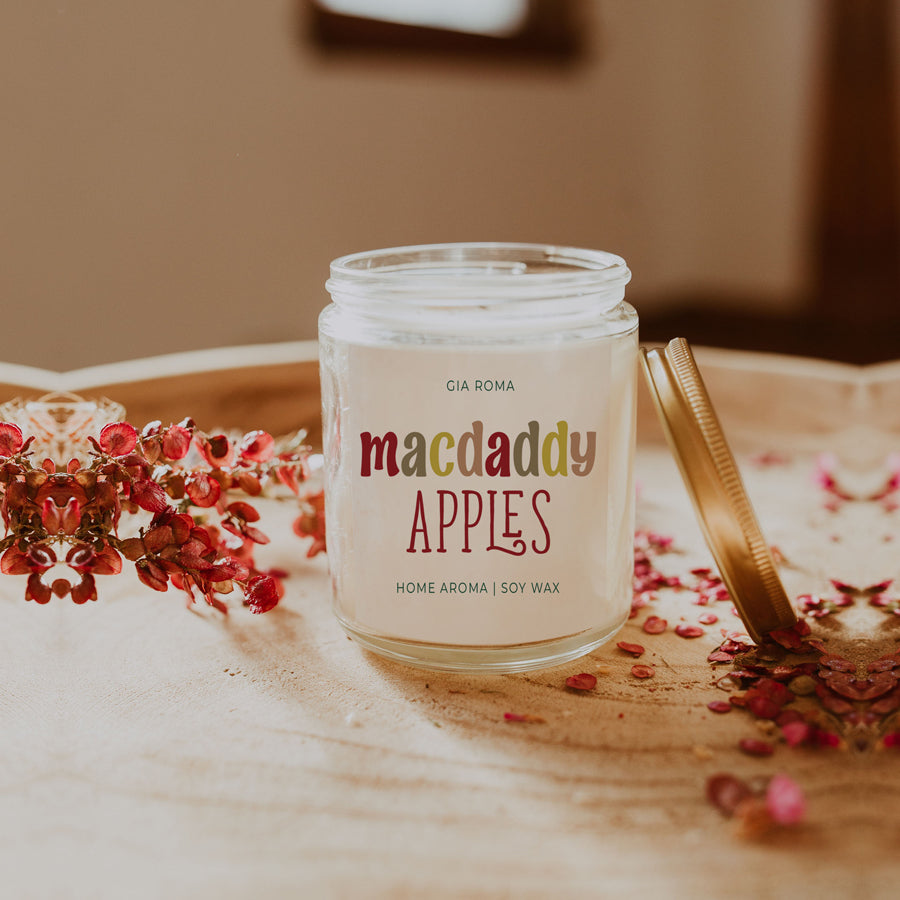 Macdaddy Apples candle with lid off on a table with dried petals