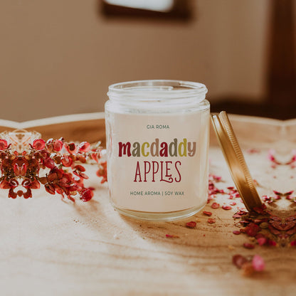 Macdaddy Apples candle with lid off on a table with dried petals