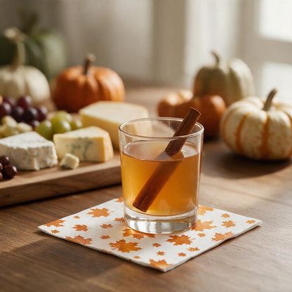 Orange foil maple leaf cocktail napkin under a glass of apple cider with a cinnamon stick at a fall party